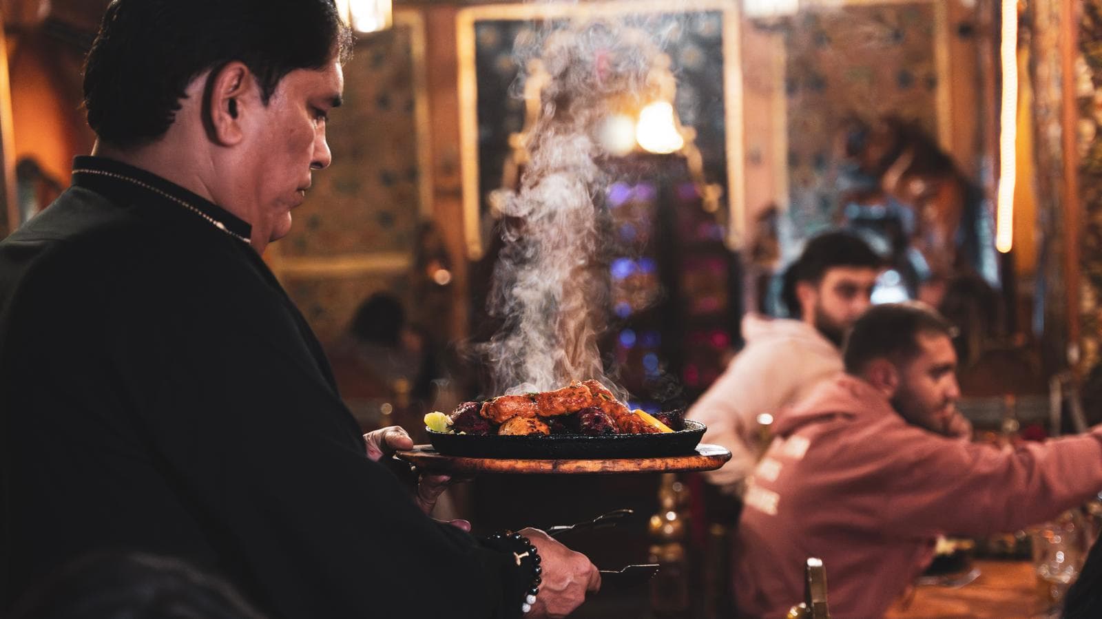 Serveur portant un sizzler fumant à travers la salle aux boiseries peintes, pendant le service du soir