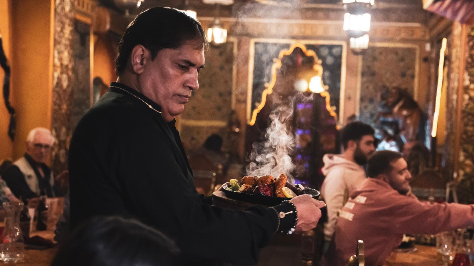 Serveur traversant la salle aux décors moghols d'O'Pakistan avec un sizzler fumant