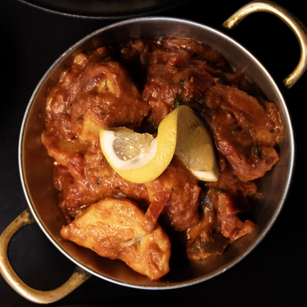 Poulet mijoté en sauce tomate crémeuse, servi en karahi avec des quartiers de citron