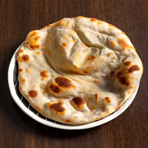 Naan doré et gonflé, tacheté par la cuisson, servi dans une assiette