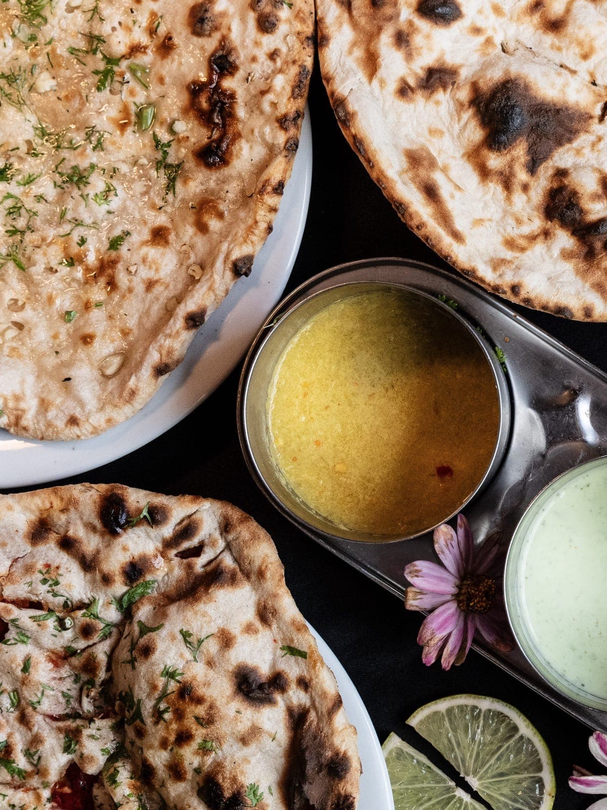 Assortiment de naans indiens garnis de coriandre servis avec des sauces dal et raita