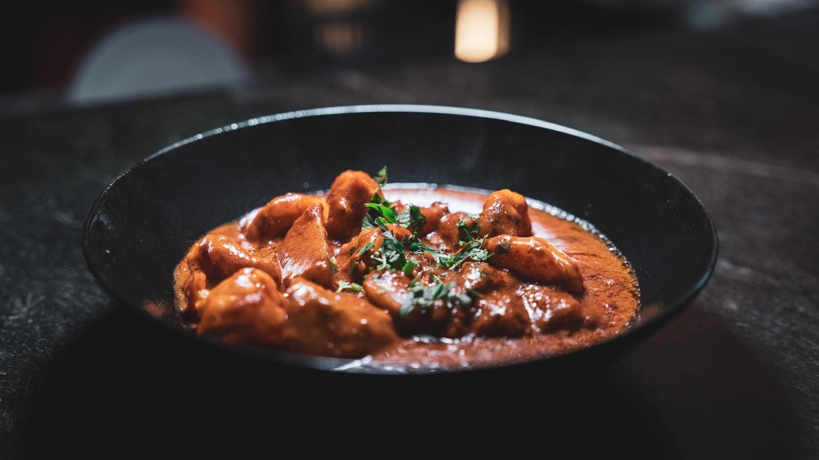 Curry de poulet halal en sauce tomate épicée, garni de coriandre, servi chez O'Pakistan