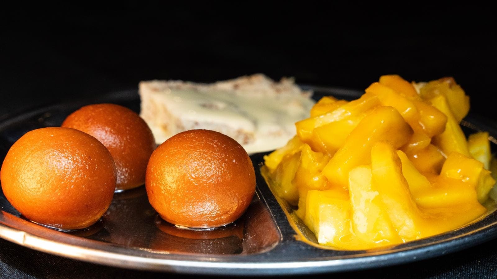 Plateau de desserts indiens avec gulab jamun, morceaux de mangue et une part de barfi