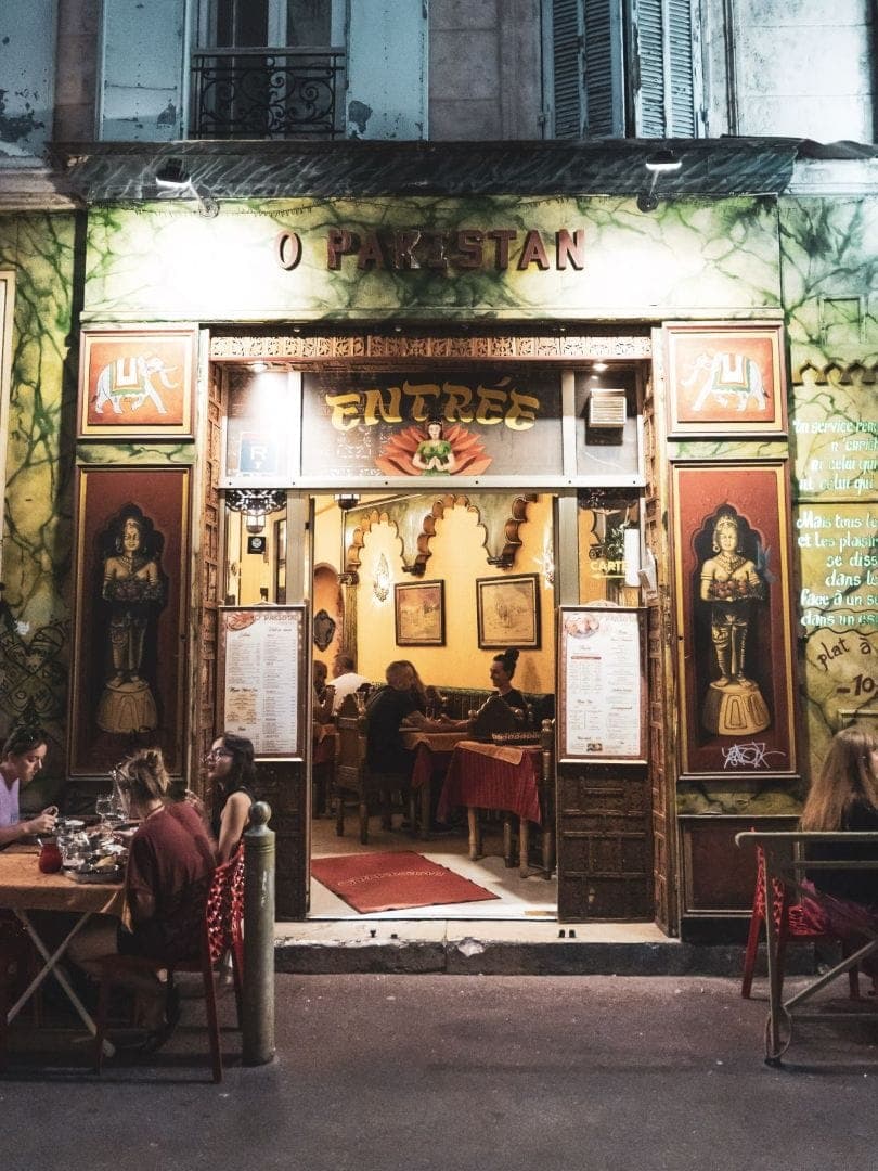 Façade colorée illuminée du restaurant O'Pakistan en soirée, avec des clients attablés en terrasse