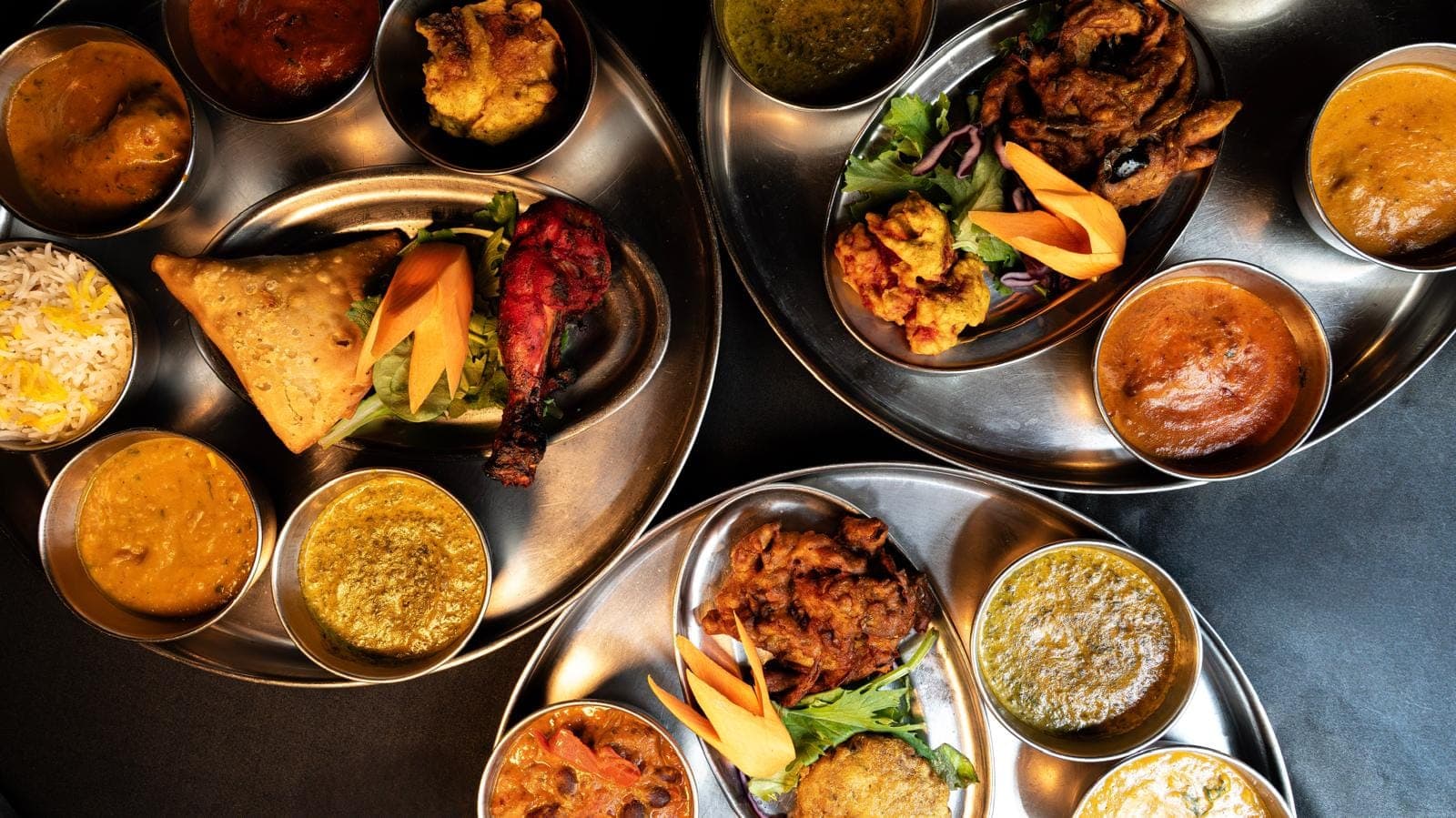 Trois thalis indiens en plongée sur plateaux en inox : currys, dal, riz basmati et accompagnements