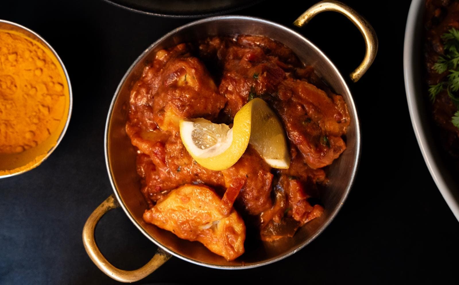 Curry de poulet en sauce tomate épicée servi dans un karahi en inox aux poignées dorées