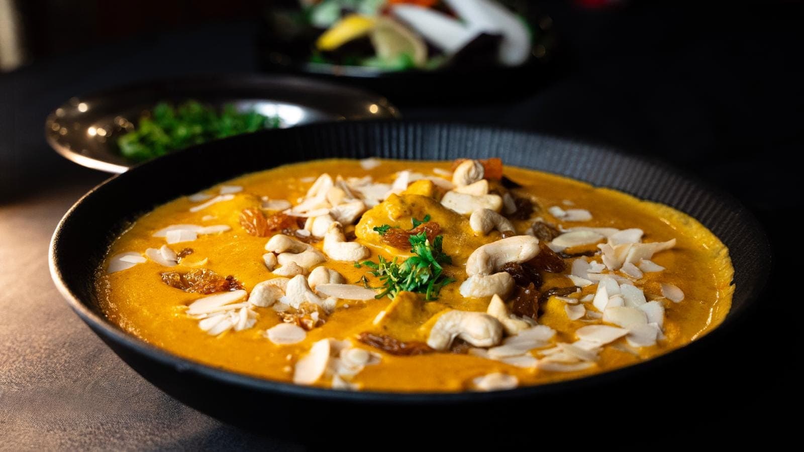 Murgh Korma crémeux parsemé de noix de cajou, d'amandes effilées et de raisins secs