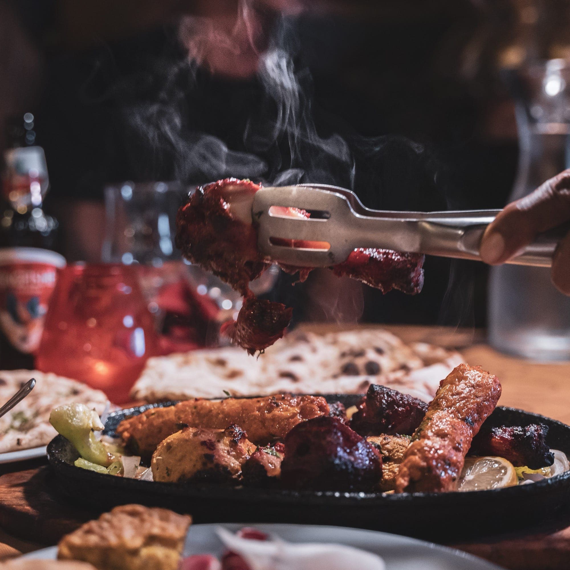 Une main saisit avec une pince une pièce de viande grillée fumante au-dessus d'un plateau