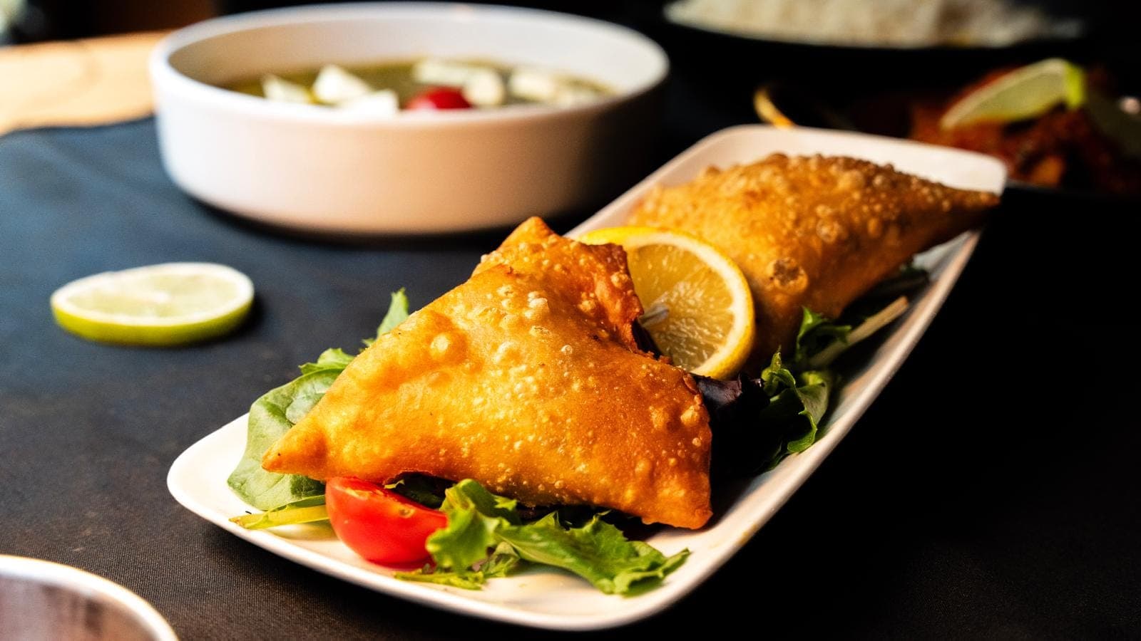 Deux samossas frits dorés sur un lit de salade avec tomates cerises et citron